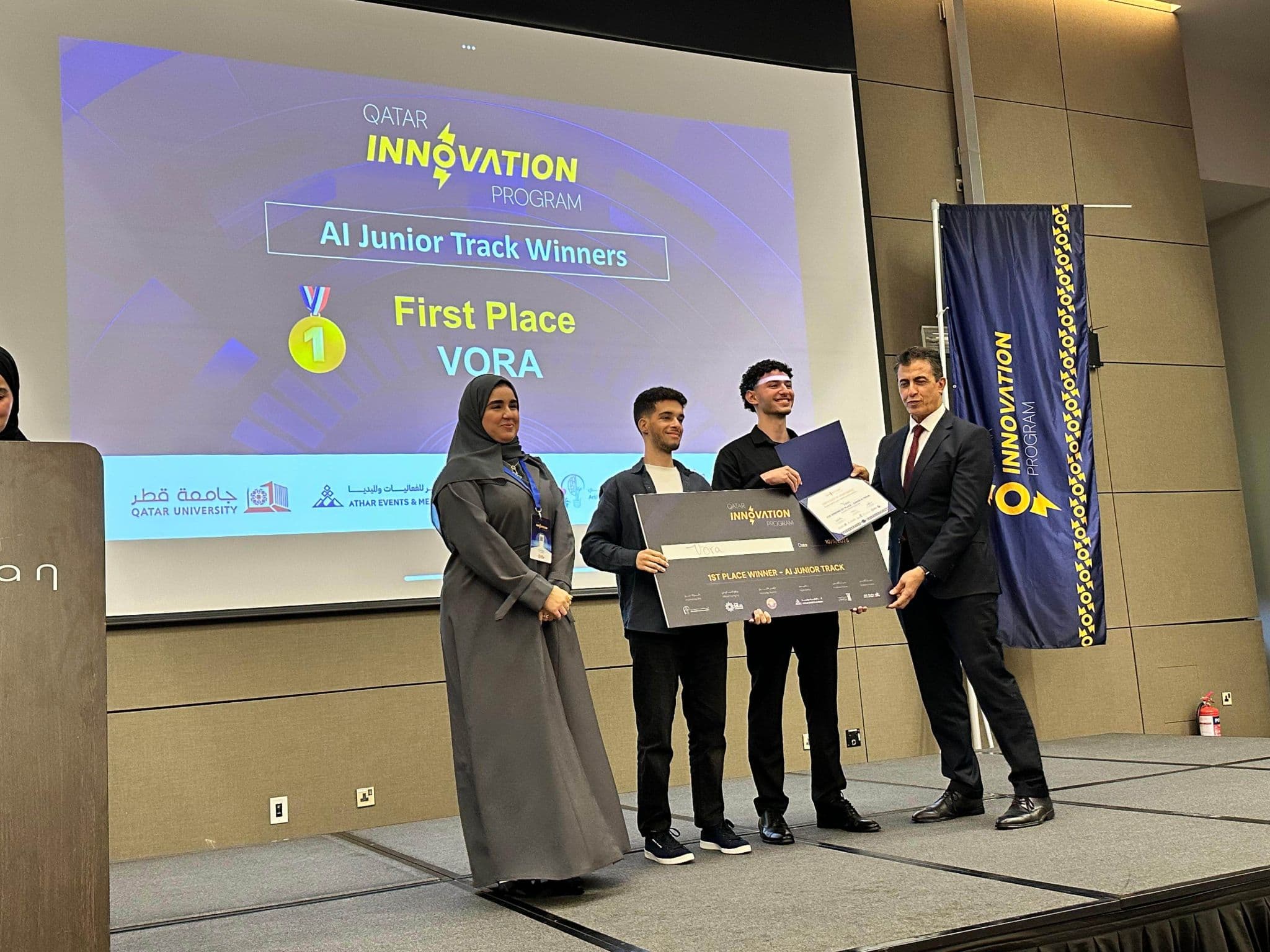 Vora team accepting the First Place award at the Qatar Innovation Program AI Junior Track on stage.